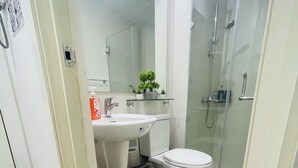 Een badkamer met toilet, wastafel en douche. Er liggen twee tapijten op de vloer.