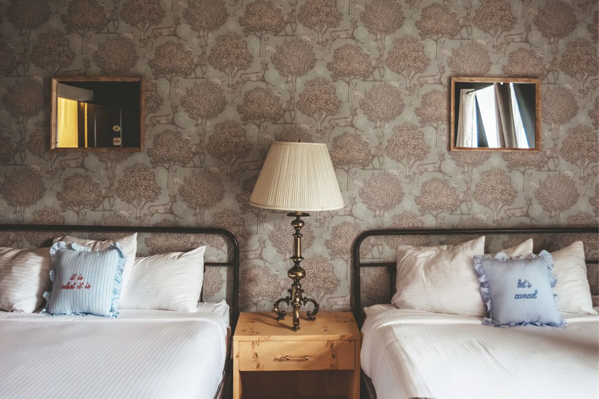 A hotel room with two beds, a nightstand, a lamp, and two wall-mounted mirrors.