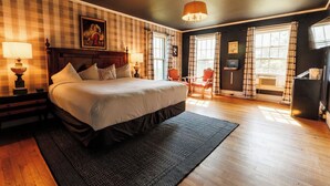 A bedroom with a large bed, two bedside tables with lamps, a headboard, a window with curtains, a chair, and a small table with a lamp. - Hideaway Inn Franconia Notch (Sugar Hill)