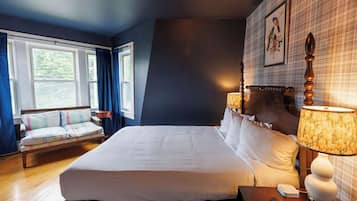 Een hotelkamer met een groot bed, een nachtkastje met lamp, een bank met kussens, en een raam met gordijnen.