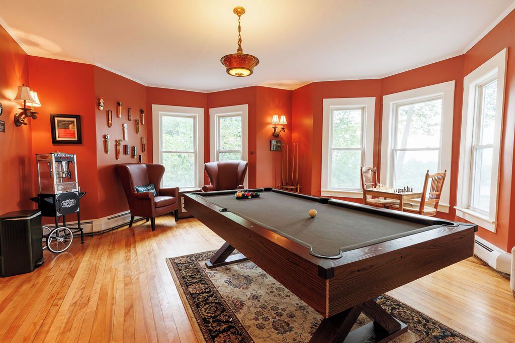 A pool table in a room with large windows, a chandelier, and wall-mounted lamps.