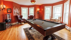 A pool table in a room with large windows, a chandelier, and wall-mounted lamps. - Hideaway Inn Franconia Notch (Sugar Hill)