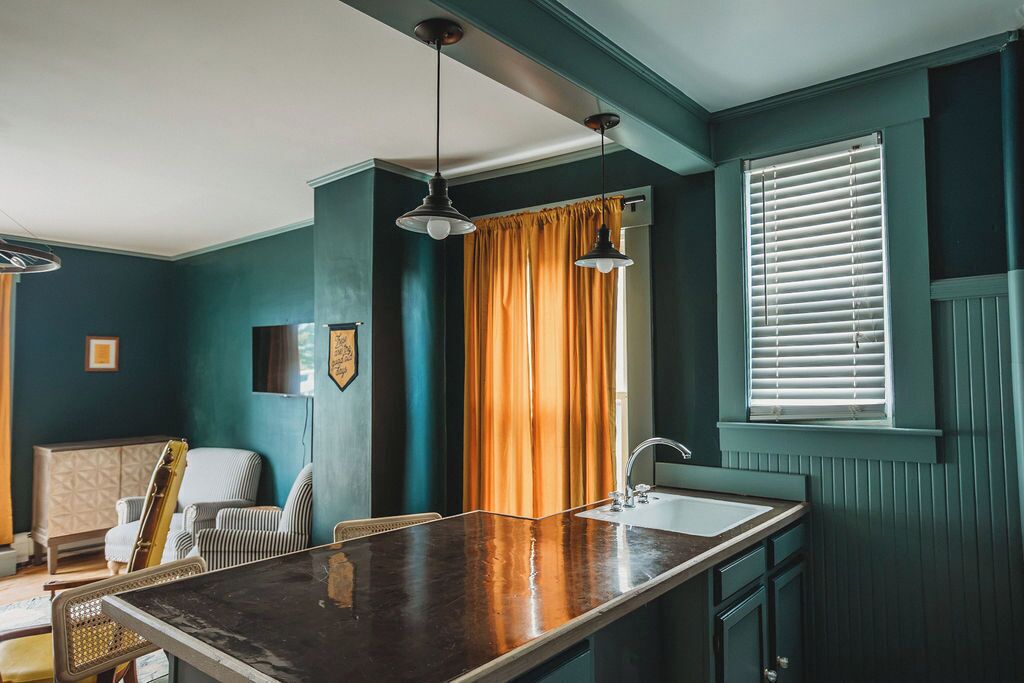A room with teal walls, a wooden bar counter, a sink, a chair, and a window with blinds.
