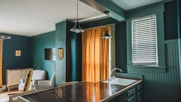 A room with teal walls, a wooden bar counter, a sink, a chair, and a window with blinds.
