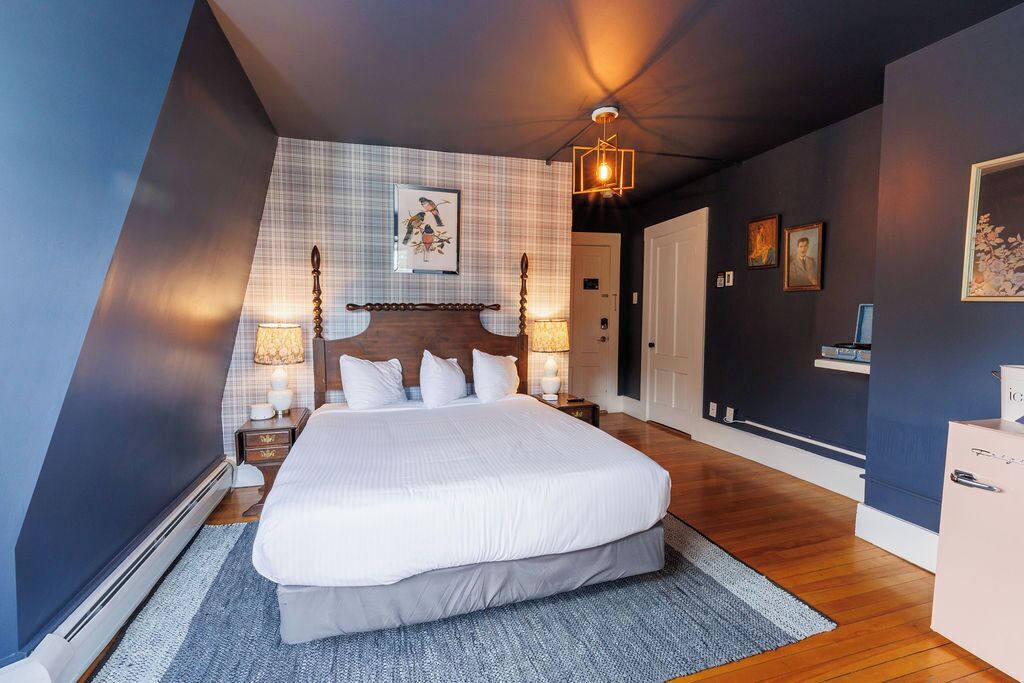 Un dormitorio moderno con una cama grande, cabecera con detalles de madera, una obra de arte en la pared y una lámpara del techo.