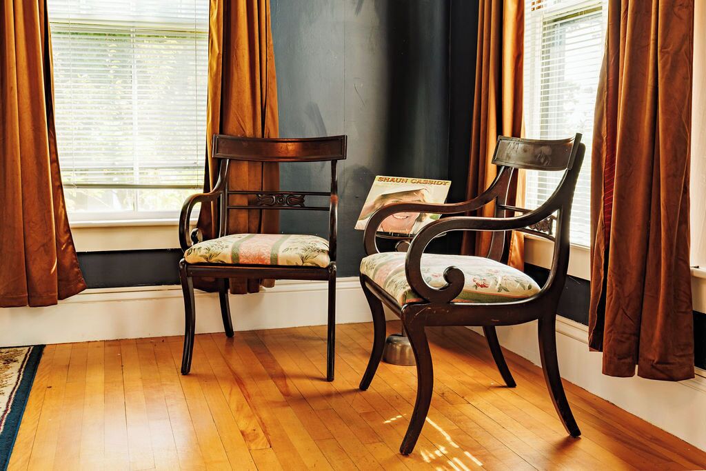 A room with two wooden chairs, a window with blinds, and a magazine on one of the chairs.