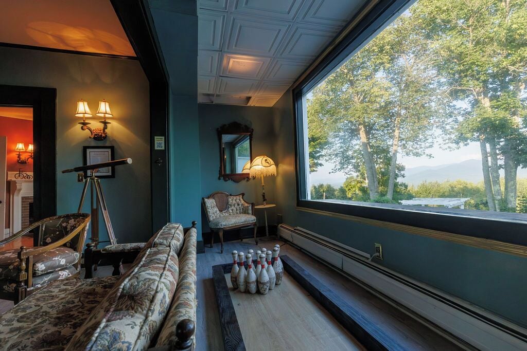 A room with a large window, a bowling alley setup, and a vintage chair.