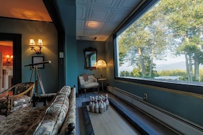 Una habitación con un ventanal grande, una zona de bolos y una silla antigua.
