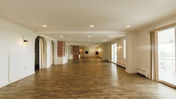 A long, open hallway with wooden flooring, white walls, and large windows on one side.