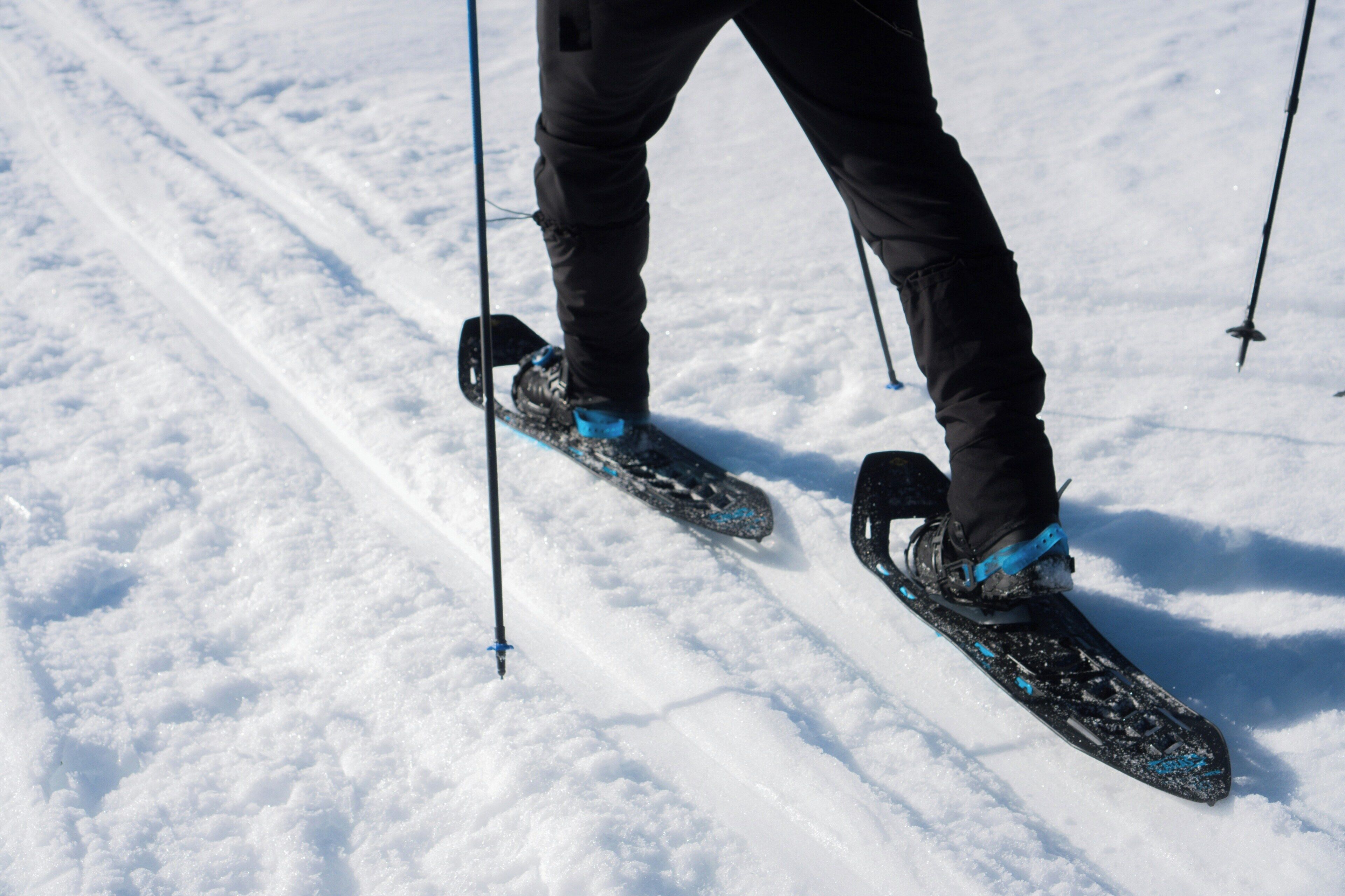 A person skiing with poles, wearing black pants and blue ski boots, on a snowy slope.