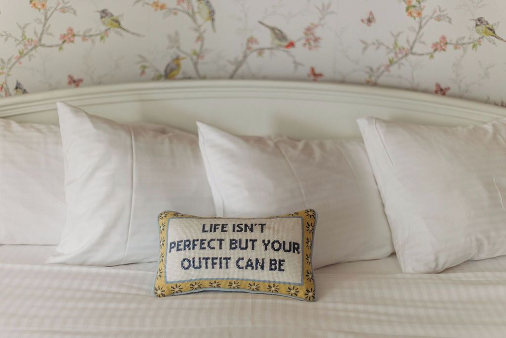 A bed with white bedding and a decorative pillow with a floral pattern and text.