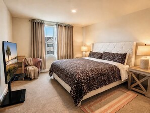 A hotel room with a bed, a TV, a chair, a window with curtains, and a nightstand with a lamp. - Modern Greenville Townhome 3BR, 3BA, Arden Woods (Greenville)