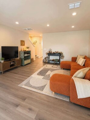 A living room with a flat-screen TV, a sofa, a fireplace, and a staircase leading to another room. - Modern Greenville Townhome 3BR, 3BA, Arden Woods (Greenville)