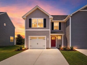 Een woonhuis met twee verdiepingen, een garage, een rode voordeur en een verzorgd gazon.