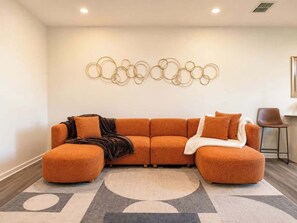 A modern living room with a sectional sofa, a decorative wall piece, and a small side table. - Modern Greenville Townhome 3BR, 3BA, Arden Woods (Greenville)