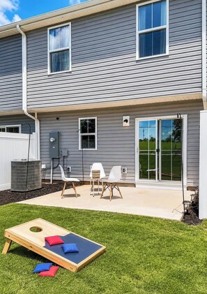 A residential building with a covered patio area, outdoor seating, and a lawn game setup. - Modern Greenville Townhome 3BR, 3BA, Arden Woods (Greenville)
