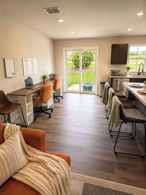 A home office with a desk, chairs, and a laptop. There is a sliding glass door leading to a patio with a lawn and trees. - Modern Greenville Townhome 3BR, 3BA, Arden Woods (Greenville)
