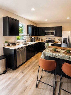 A modern kitchen with black cabinets, stainless steel appliances, and a central island with bar stools. - Modern Greenville Townhome 3BR, 3BA, Arden Woods (Greenville)
