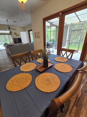 A dining area with a table set for four, surrounded by wooden chairs, a television, and a grill outside.
