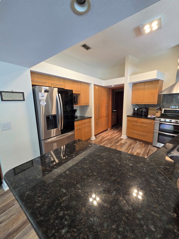 A modern kitchen with stainless steel appliances, wooden cabinets, and a granite countertop.