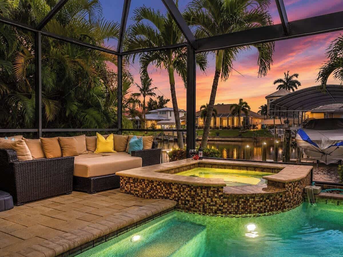 A pool area with a hot tub, a sofa, and a view of a body of water and palm trees.
