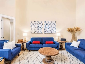 Ein Wohnzimmer mit blauem Sofagarnitur, einem runden Couchtisch und zwei Wandleuchten.