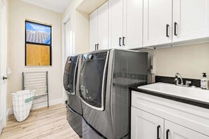 A compact kitchen with a built-in washer and dryer, a sink, and a window with a view of a building. - THE Luxury Villa, Gulf Access, Pool, Spa, Tiki Hut (Cape Coral)