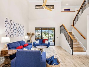 A spacious living room with a blue sofa set, a coffee table, and a staircase with wooden steps and black railings. - THE Luxury Villa, Gulf Access, Pool, Spa, Tiki Hut (Cape Coral)