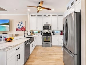 A modern kitchen with white cabinetry, stainless steel appliances, a marble countertop, and a ceiling fan.