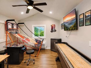 A room with a slingshot, a ping pong table, a desk, and a window with a view of greenery. - Luxe 2BR Cabin Private Pickleball, Hot Tub, Golf (Pigeon Forge)