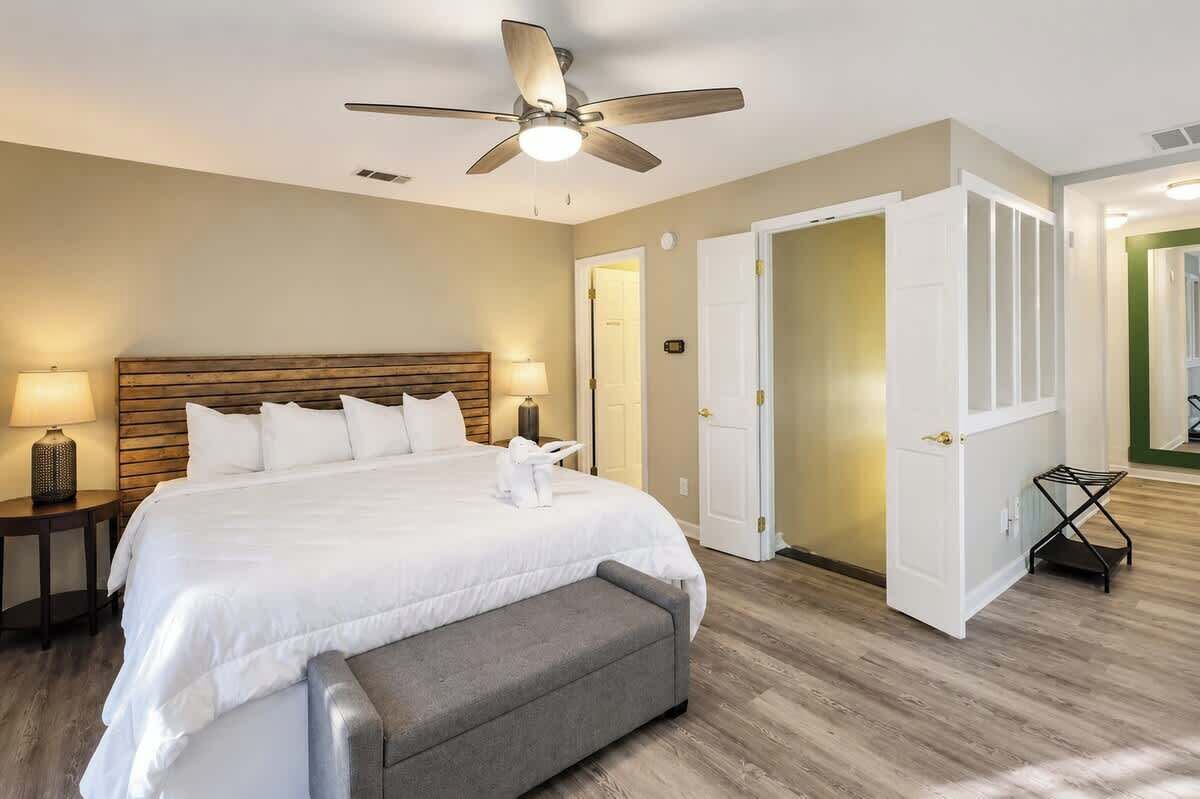 A hotel room with a bed, a ceiling fan, a nightstand, and a bench.