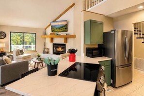 A modern kitchen with a stainless steel refrigerator, a flat-screen TV mounted above the fireplace, and a dining area with a marble countertop. - Luxe 2BR Cabin Private Pickleball, Hot Tub, Golf (Pigeon Forge)