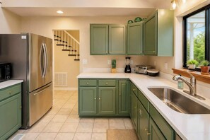 A kitchen with green cabinets, a stainless steel refrigerator, a built-in oven, a sink, and a window with a view of greenery. - Luxe 2BR Cabin Private Pickleball, Hot Tub, Golf (Pigeon Forge)