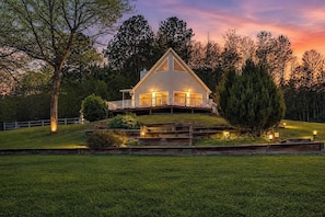 A two-story house with a balcony, surrounded by a well-maintained lawn and trees. - Luxe 2BR Cabin Private Pickleball, Hot Tub, Golf (Pigeon Forge)