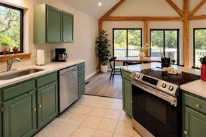A kitchen with green cabinets, a stainless steel dishwasher, a black stove, and a large window overlooking a deck. - Luxe 2BR Cabin Private Pickleball, Hot Tub, Golf (Pigeon Forge)