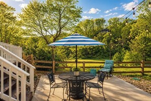 A patio with a round table, chairs, and a blue-striped umbrella. - Luxe 2BR Cabin Private Pickleball, Hot Tub, Golf (Pigeon Forge)