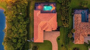 An aerial view of a property with a swimming pool, a large covered patio, and a separate building with a tiled roof. - Naples Luxury Home, Resort Pool, Lanai, Fire Table (Naples)
