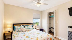Ein Schlafzimmer mit Bett, Nachttischen, Deckenventilator, Fenster mit Jalousien und einem Kleiderschrank.