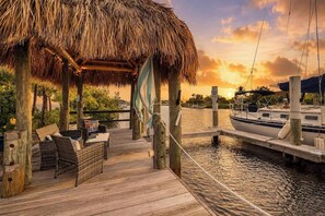 A wooden dock with a thatched roof seating area overlooking a calm body of water, with a boat docked to the right. - Port Charlotte Waterfront Luxe Tiki, Pool, Dock (Port Charlotte)