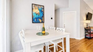 Ein Essbereich mit einem weißen Tisch, sechs Stühlen, einer Champagnerflasche und einem gerahmten abstrakten Gemälde an der Wand.