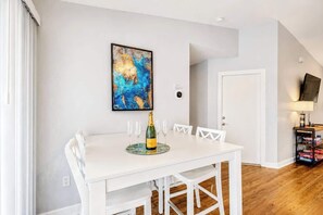 A dining area with a white table, six chairs, a bottle of champagne, and a framed abstract painting on the wall. - Port Charlotte Waterfront Luxe Tiki, Pool, Dock (Port Charlotte)
