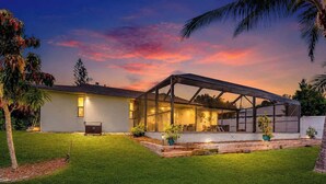 Ein modernes Haus mit überdachter Terrasse, einem gepflegten Rasen und einem Sonnenuntergangshimmel.