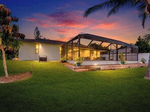A modern house with a covered patio, a well-maintained lawn, and a sunset sky. - Port Charlotte Waterfront Luxe Tiki, Pool, Dock (Port Charlotte)