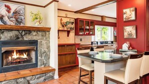 A kitchen with a stone fireplace, wooden cabinets, and a dining area with chairs. - Secluded Mountain Paradise, Hot Tub, Firepit, View (Sevierville)