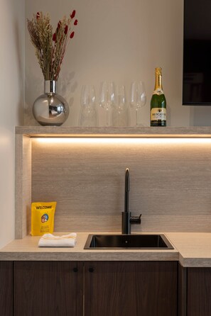 Eine moderne Küche mit integriertem Spülbecken, einer Vase mit Trockenblumen, einer Champagnerflasche und einem Willkommenspaket.