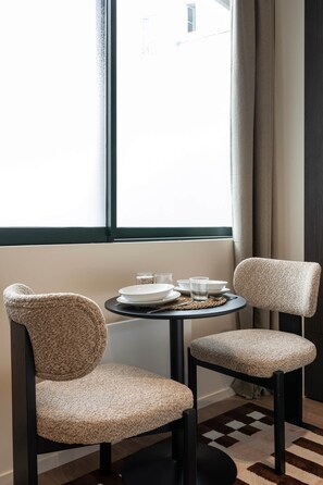 Ein Zimmer mit zwei Stühlen, einem kleinen Tisch und einem Fenster mit Vorhängen.