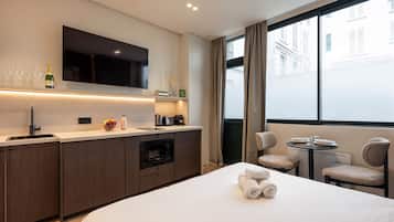 Habitación de hotel moderna con kitchenette, cama con toallas, televisor y vista a la ciudad.