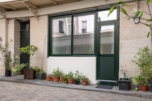 A building facade with a large window, multiple potted plants, and a door. - Elegant Studio in the Vendôme - Madeleine Area (Paris)