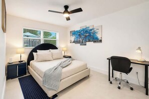 Ein Schlafzimmer mit einem Bett, einem Schreibtisch, einem Sessel, einem Deckenventilator und Kunstwerken an der Wand.