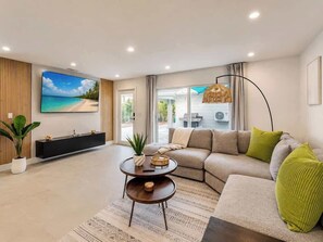 Ein modernes Wohnzimmer mit einer Couch, einem Couchtisch, einem an der Wand befestigten Fernseher und einem großen Fenster.